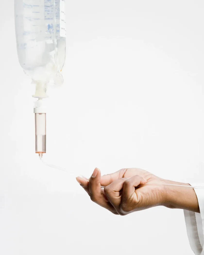 A clinician's hand holding the line below an IV fluid bag and drip chamber