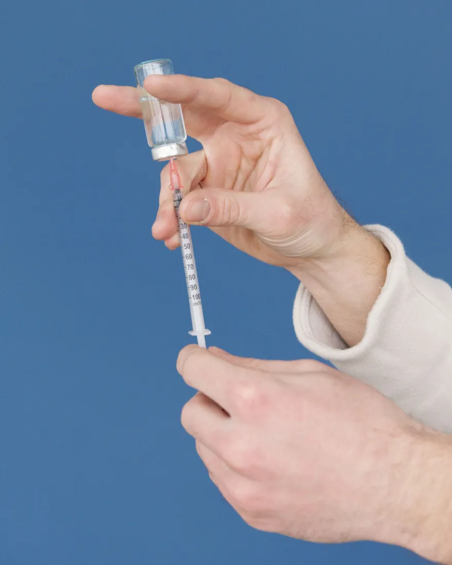 Hands drawing a dose from a medication vial with a syringe